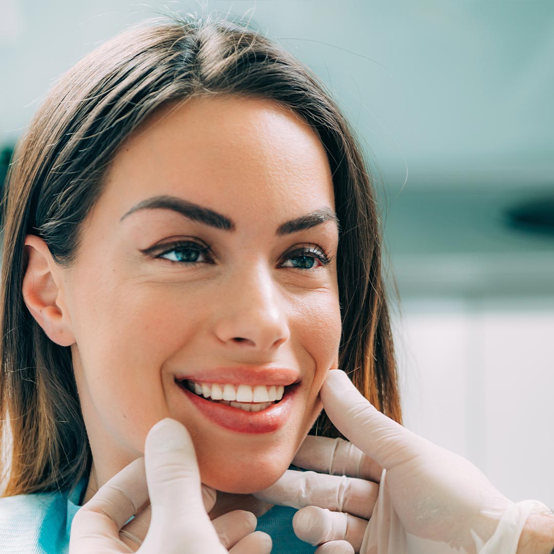 The image shows a woman seated in a dental chair, smiling broadly, with a dental professional adjusting her braces.