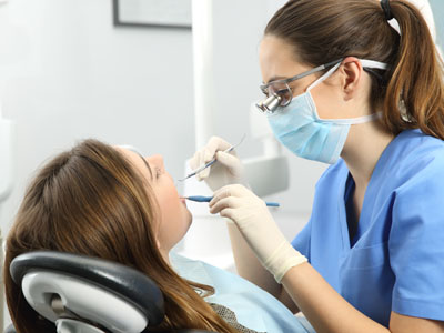 A dental hygienist performing a cleaning procedure on a patient s teeth while wearing personal protective equipment.
