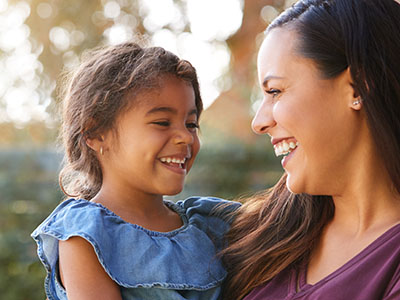 The image shows a woman and a child sharing a joyful moment outdoors, with both smiling.