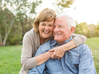A man and woman are embracing each other outdoors, with both smiling and looking at the camera.