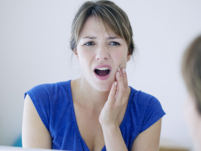 The image shows a woman with her mouth open, possibly expressing surprise or concern, looking at her reflection in a mirror while making a face.