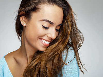 This is a split-screen image featuring a woman on the left with long hair smiling at the camera, looking down slightly, wearing a blue top, against a white background  on the right, the same woman appears with her eyes closed, smiling broadly, and looking upwards, also in a blue top.