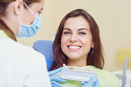 A woman with a dental device in her mouth is smiling at the camera while a dental professional attends to her.