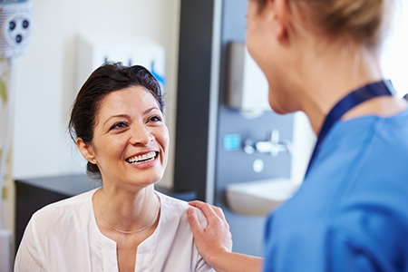 The image shows two individuals  on the left, there s a woman with her arm around another person, who appears to be a medical professional, possibly a nurse or doctor, standing in what looks like a healthcare setting, likely an examination room.