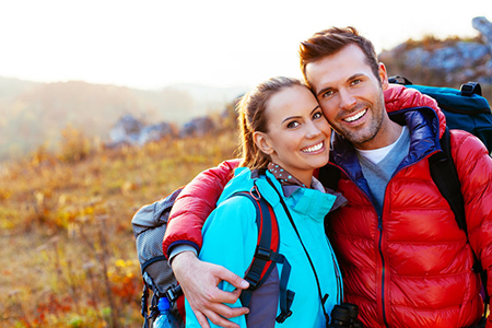 Two people posing together in an outdoor setting with backpacks, smiling at the camera, during daylight.