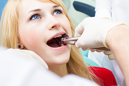 A woman receiving dental treatment from a dentist, with her mouth open and a dental instrument being used on her teeth.
