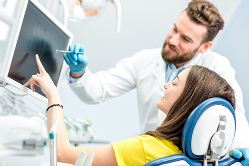 The image shows a man and woman in a medical setting, with the man wearing a stethoscope around his neck and pointing at something on a computer screen while the woman looks on attentively.