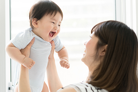 The image shows a woman holding a baby with a joyful expression, possibly smiling at the child s reaction to something.