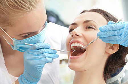 A dental hygienist performing a teeth cleaning procedure on a patient s mouth while wearing protective gloves and a mask.