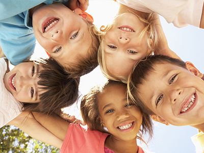 A group of children posing together with smiles, against a clear sky background.