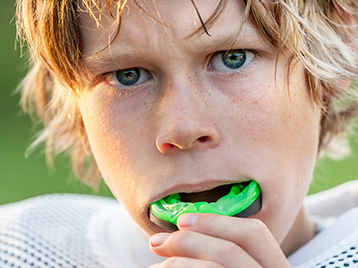 A young boy blowing bubbles with green bubble gum.