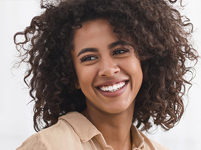 A smiling woman with curly hair and a happy expression, wearing a light-colored top.