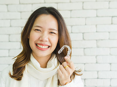 The image features a woman with a radiant smile holding up a toothbrush, standing next to another person who is also smiling. They are both indoors, possibly in a retail setting.